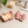 A pink silicone resin mold shaped like a bow is displayed next to a lit candle and a glass bottle.