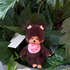 A small brown plush cartoon character with pink accents is nestled among green leaves.