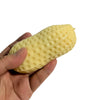 A hand is holding a yellow, bumpy peanut-shaped squishy stress ball.