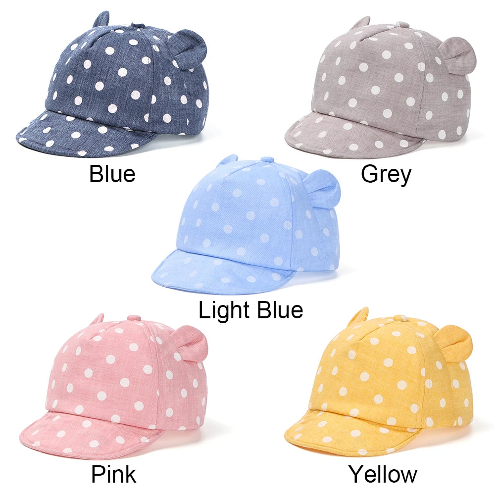 A collection of baby cotton baseball caps in blue, grey, light blue, pink, and yellow with white polka dots.