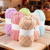Two skeins of pink and beige chunky yarn are displayed on a wooden table.