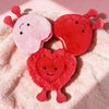 Two heart-shaped plush toys in pink and red resting on a fluffy pink background.