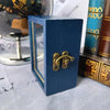A small, dark blue wooden box with brass hardware sits next to a glass globe and a stack of old books.