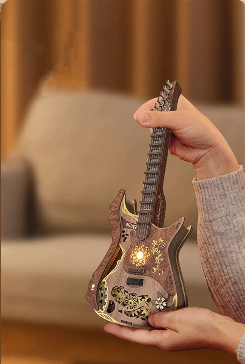 A hand holds a wooden miniature guitar model kit, showing the detailed buildable puzzle craft for music lovers.