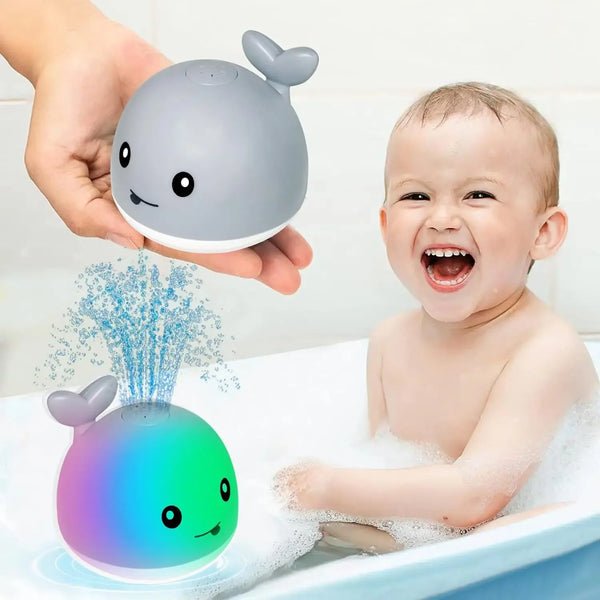 A baby is playing with a light-up whale bath toy that sprays water in a bathtub.