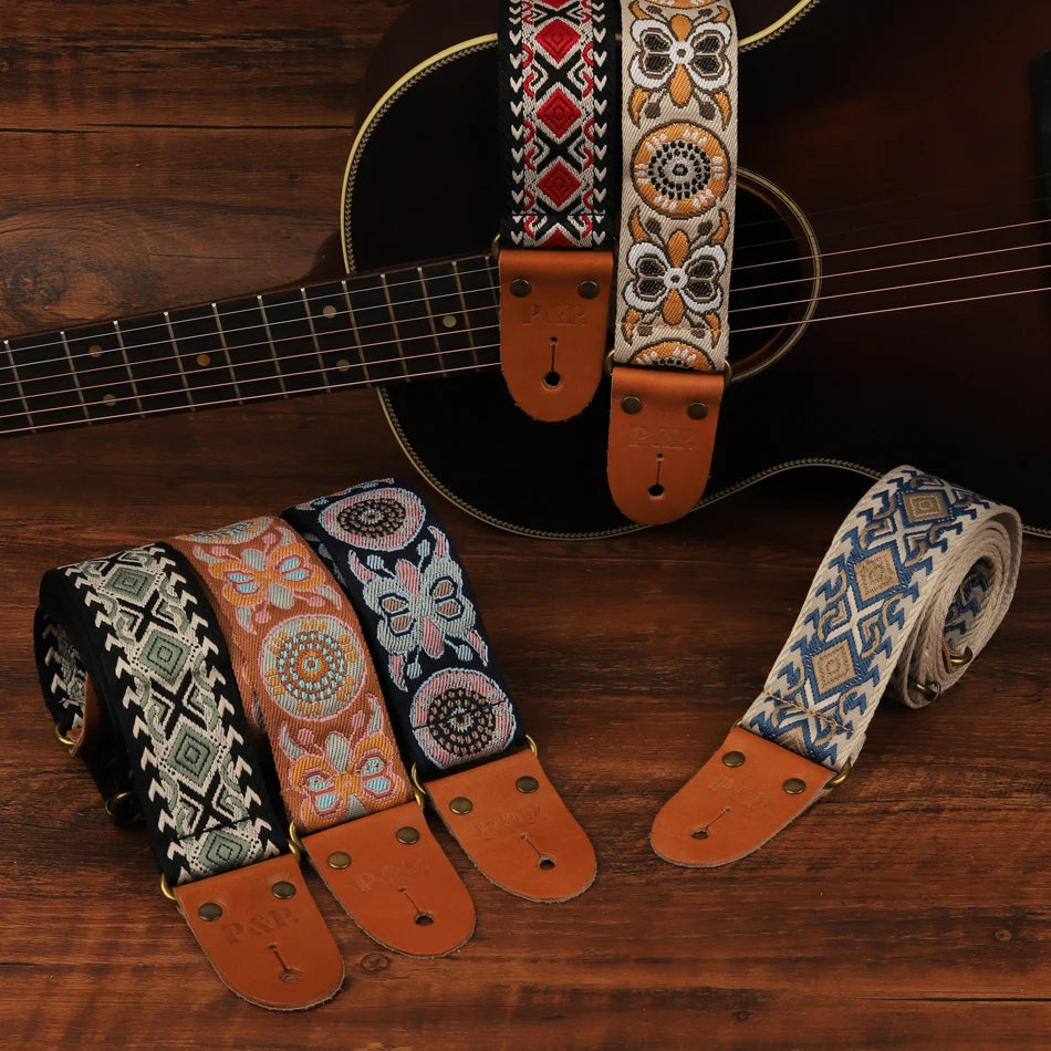 A collection of embroidered guitar straps featuring various patterns and leather ends laid out on a wooden surface.