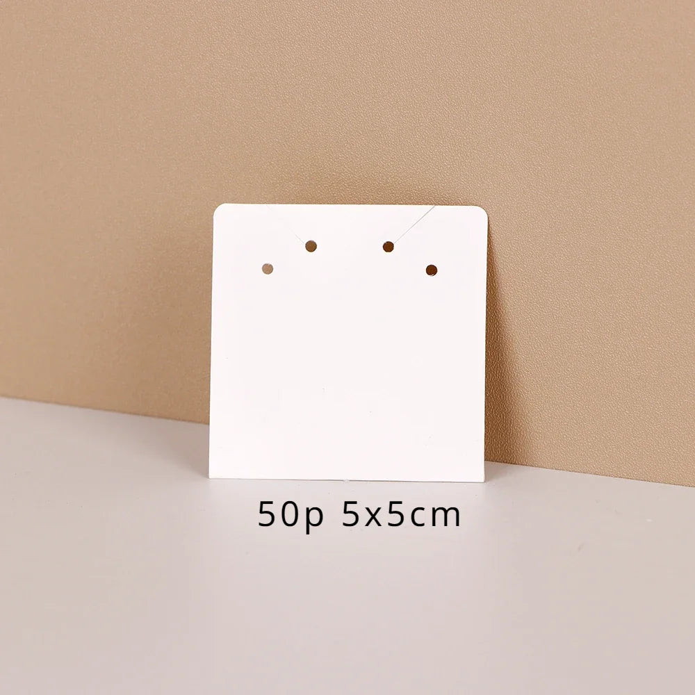 A white square jewelry display card with three holes is shown against a beige background.