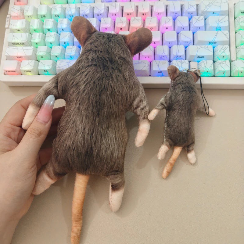 A hand holds a gray cat plush toy next to a keyboard with colorful backlighting.