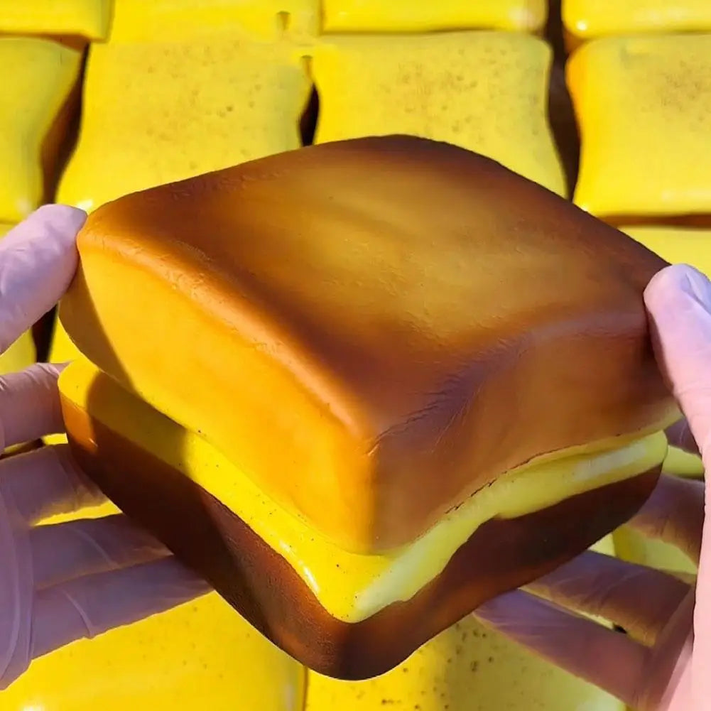 A hand holds a squishy toast stress relief toy with a golden-yellow color.
