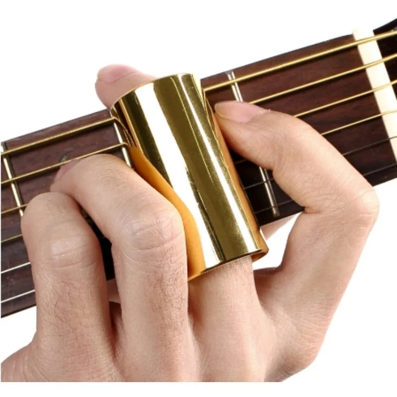 A hand holds a gold-colored precision guitar slide bar against the strings of a wooden guitar neck.