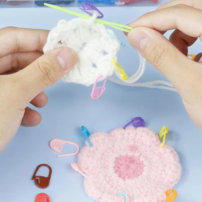Hands are holding a white yarn pom-pom with colorful locking stitch markers for knitting and crochet