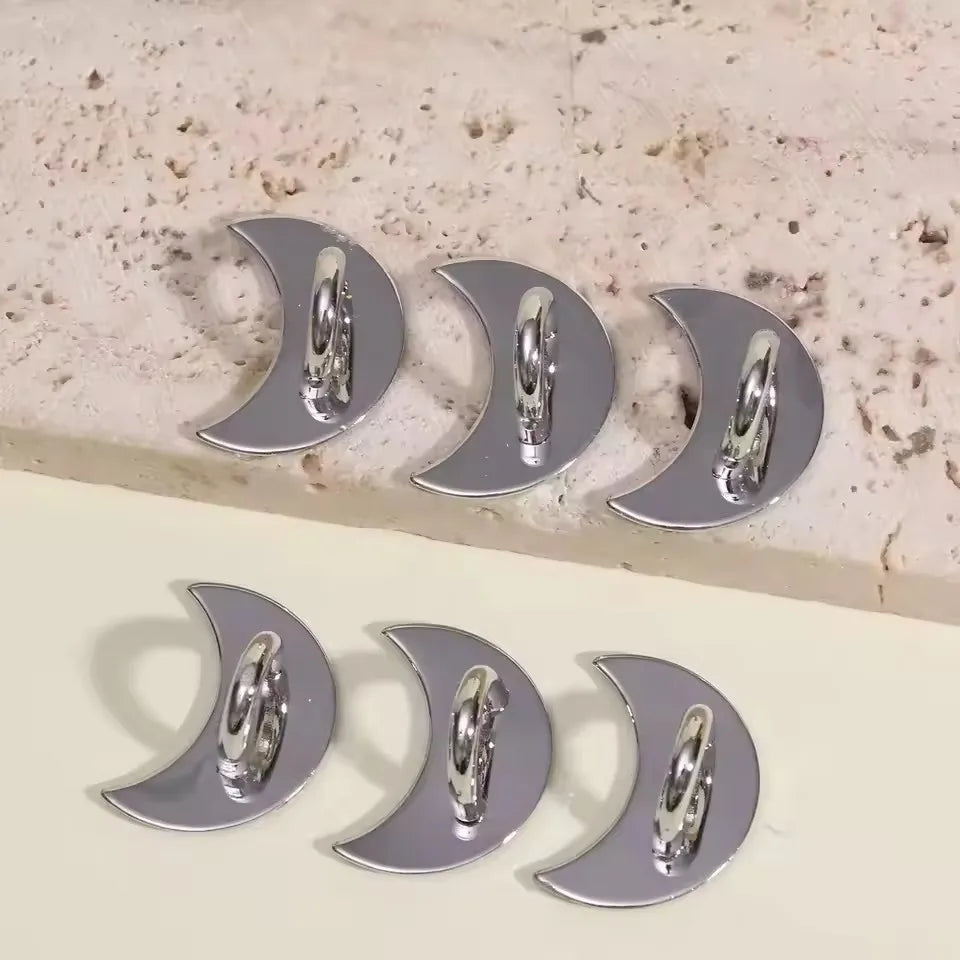 Silver decorative phone charm hooks with adhesive backing arranged on a light surface.