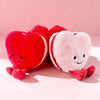 A pair of soft plush hearts, one red and one pink, resting on a light pink background.