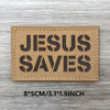 Un patch tissé beige rectangulaire avec du texte noir indiquant JESUS SAUVE sur une surface en bois patinée.