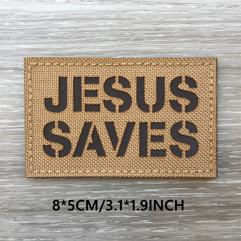 Un patch tissé beige rectangulaire avec du texte noir indiquant JESUS SAUVE sur une surface en bois patinée.
