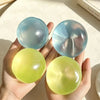 A hand holds two translucent blue silicone fidget balls, one larger and one smaller.