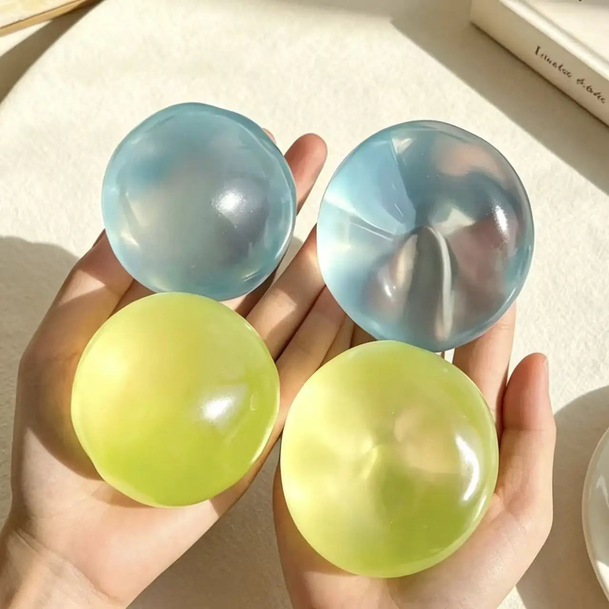 A hand holds two translucent blue silicone fidget balls, one larger and one smaller.