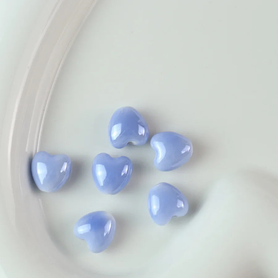 A collection of light blue heart-shaped ceramic beads scattered on a white surface.