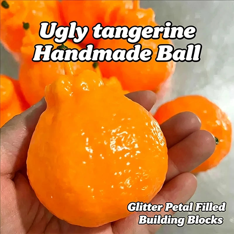 A hand holds an orange handmade ball, which is a glitter petal filled building block.