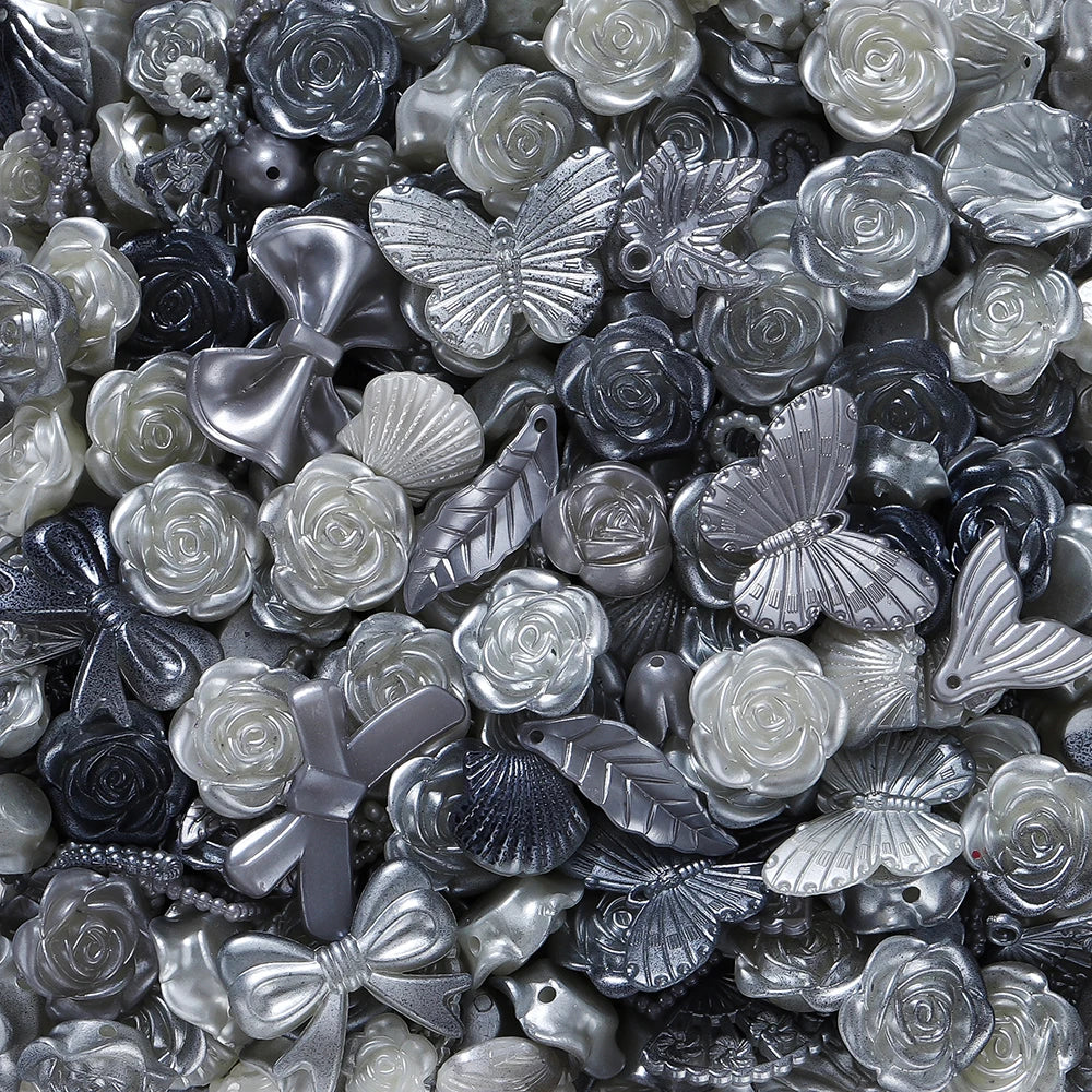 A close-up of silver and iridescent acrylic beads shaped like roses, shells, and butterflies for jewelry making.