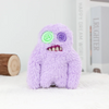 A purple, fuzzy monster plush toy with glowing green and purple eyes sits on a white surface.