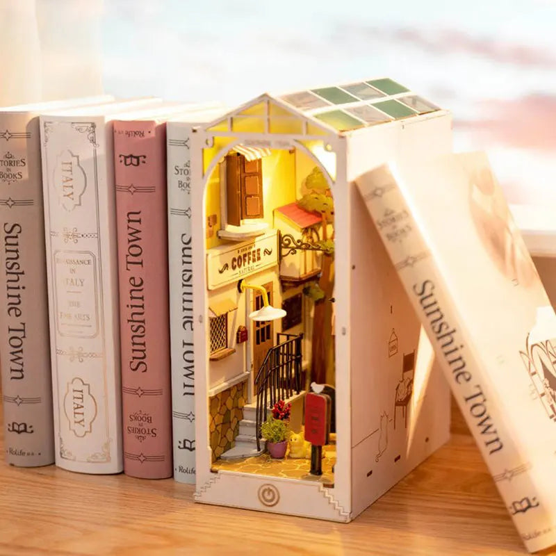 A miniature dollhouse kit of a house with an arched entrance and interior details, displayed next to books.