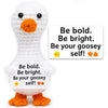A white crochet goosey self doll with orange feet and a sign that says Be bold Be bright Be your goosey self