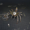 A detailed steampunk metal spider model with intricate joints and gears is displayed on a dark grid background.