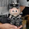 A plush Labubu doll wearing a black and gray flannel outfit with a bow, held in a person's hand.