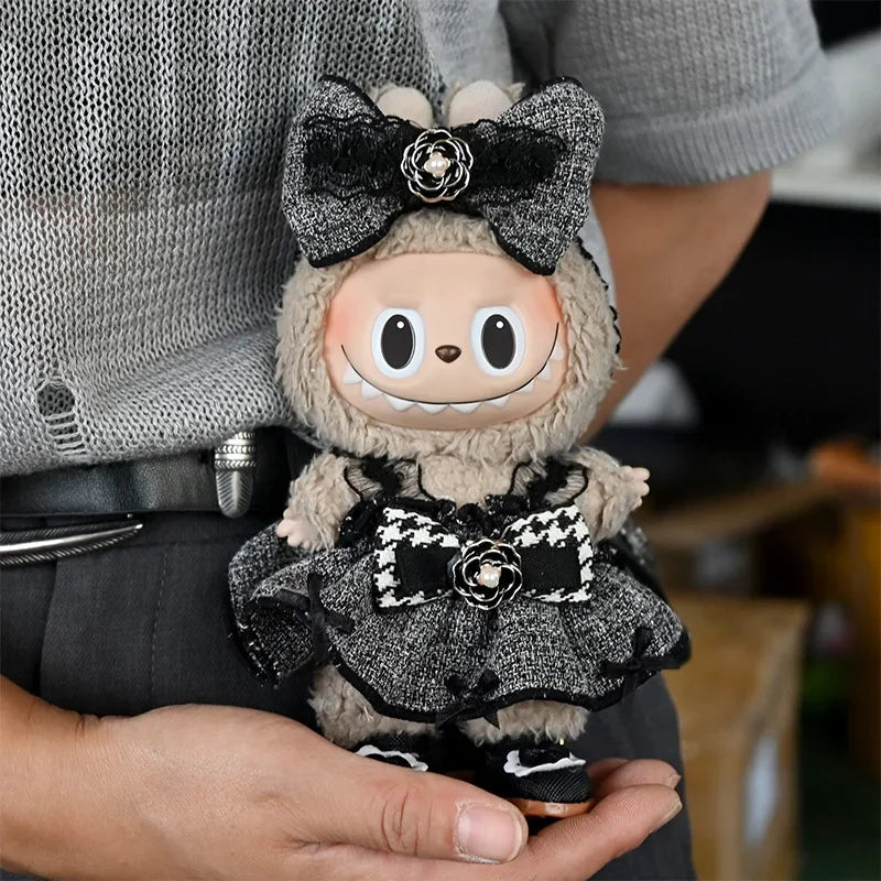 A plush Labubu doll wearing a black and gray flannel outfit with a bow, held in a person's hand.
