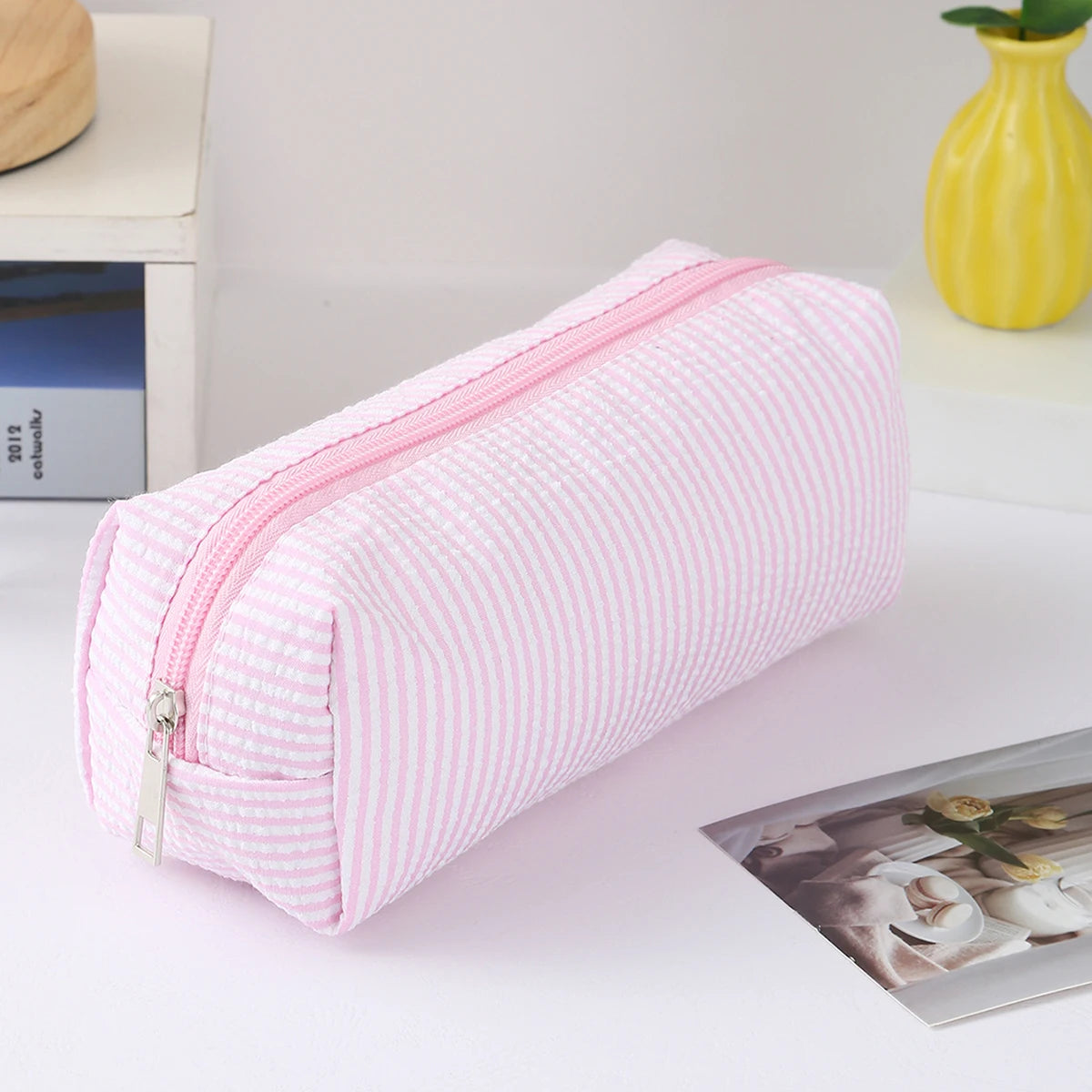 Pink and white striped canvas pencil case with a zipper, lying on a white surface.