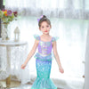 A young girl wearing a purple and teal mermaid fantasy dress with a ruffled fishtail skirt standing indoors.