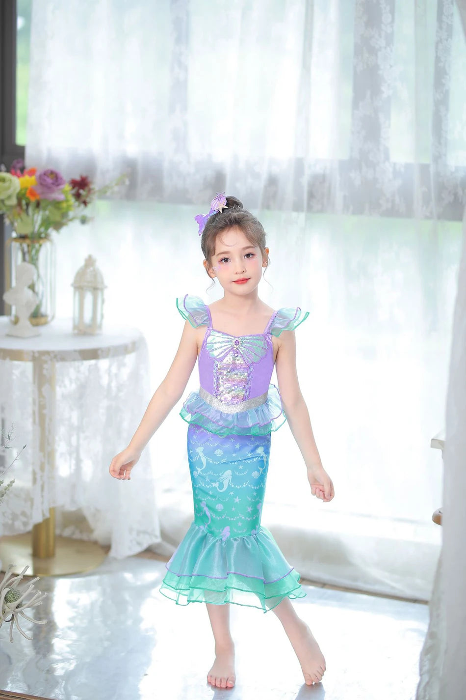 A young girl wearing a purple and teal mermaid fantasy dress with a ruffled fishtail skirt standing indoors.