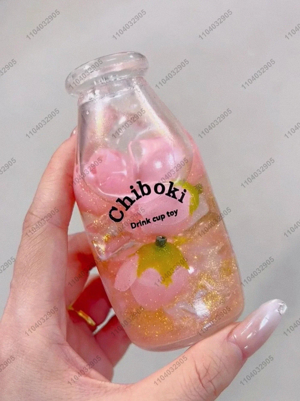 A hand holds a clear bottle filled with pink and yellow squishy fruit toys labeled Chiboki