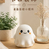 A white, squishy ghost-shaped stress ball is placed on a wooden surface next to some dried flowers.