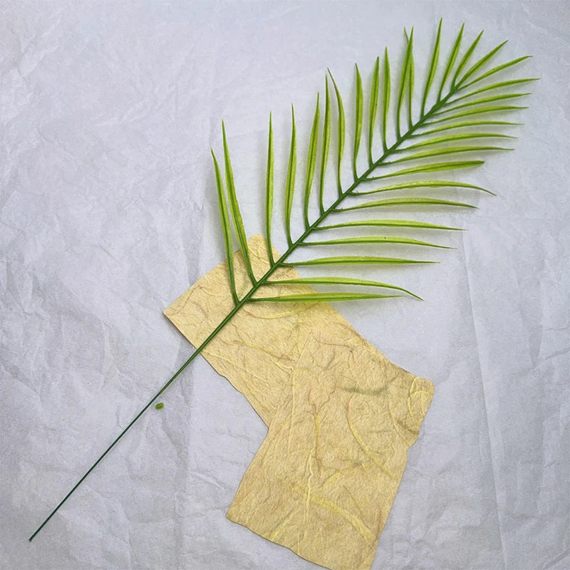 A vibrant green palm frond rests on a piece of yellow, textured paper.