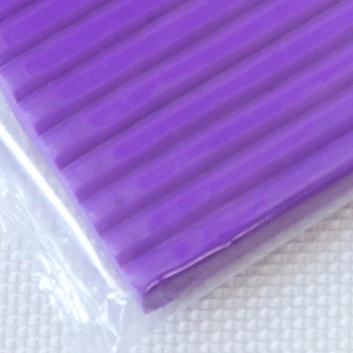 A purple block of soft modeling clay with ribbed texture is shown against a white background.