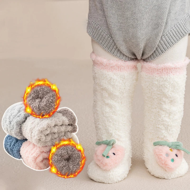A pair of white fuzzy baby knee-high socks with pink trim and a small green accent, displayed next to a plush toy.