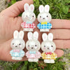 A hand holds several cute white rabbit resin bead charms with colorful plaid bows and accents.