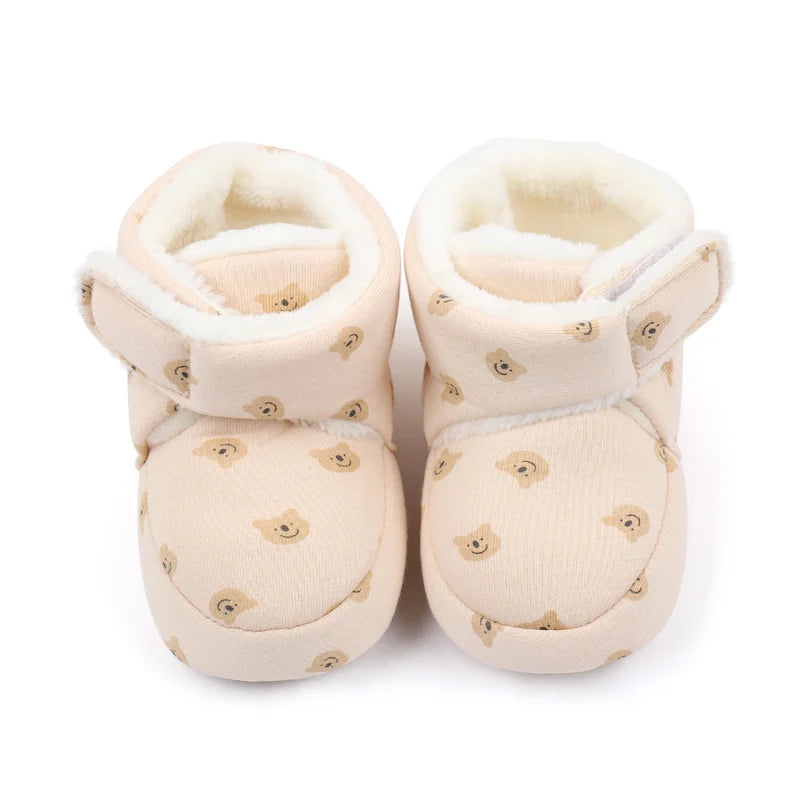 Pair of light beige baby winter snow boots with fuzzy ball accents