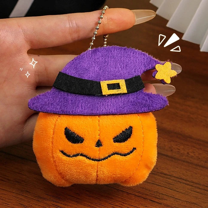 A purple witch hat and orange pumpkin plush keychain set with a yellow bat charm being held by a hand.