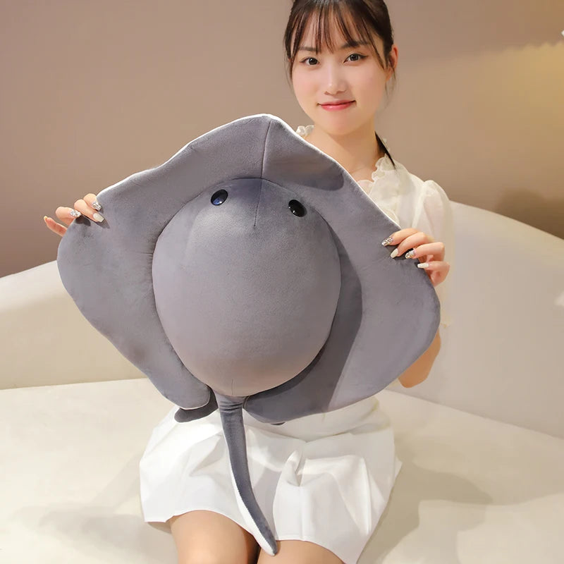 A woman holds a gray plush toy shaped like a ray devil fish, which is a soft stuffed ocean animal pillow.