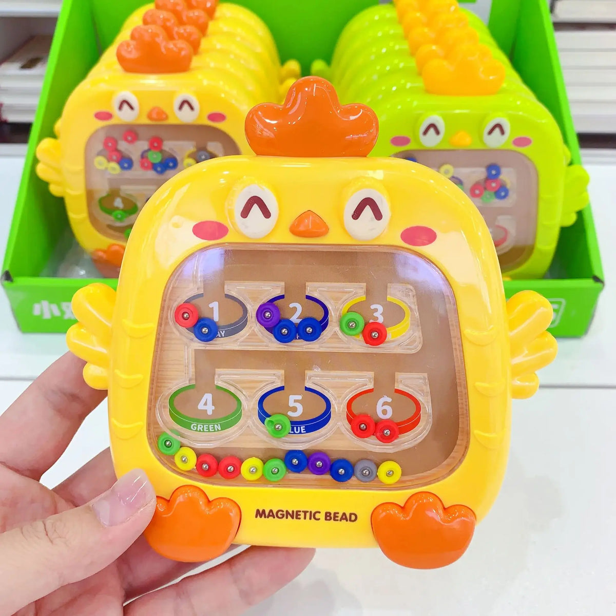 A yellow magnetic bead puzzle board for toddlers with numbered holes and colored beads, held in a hand.