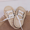 A pair of light beige wooden lacing shoes for fine motor skill development resting on a textured brown fabric.