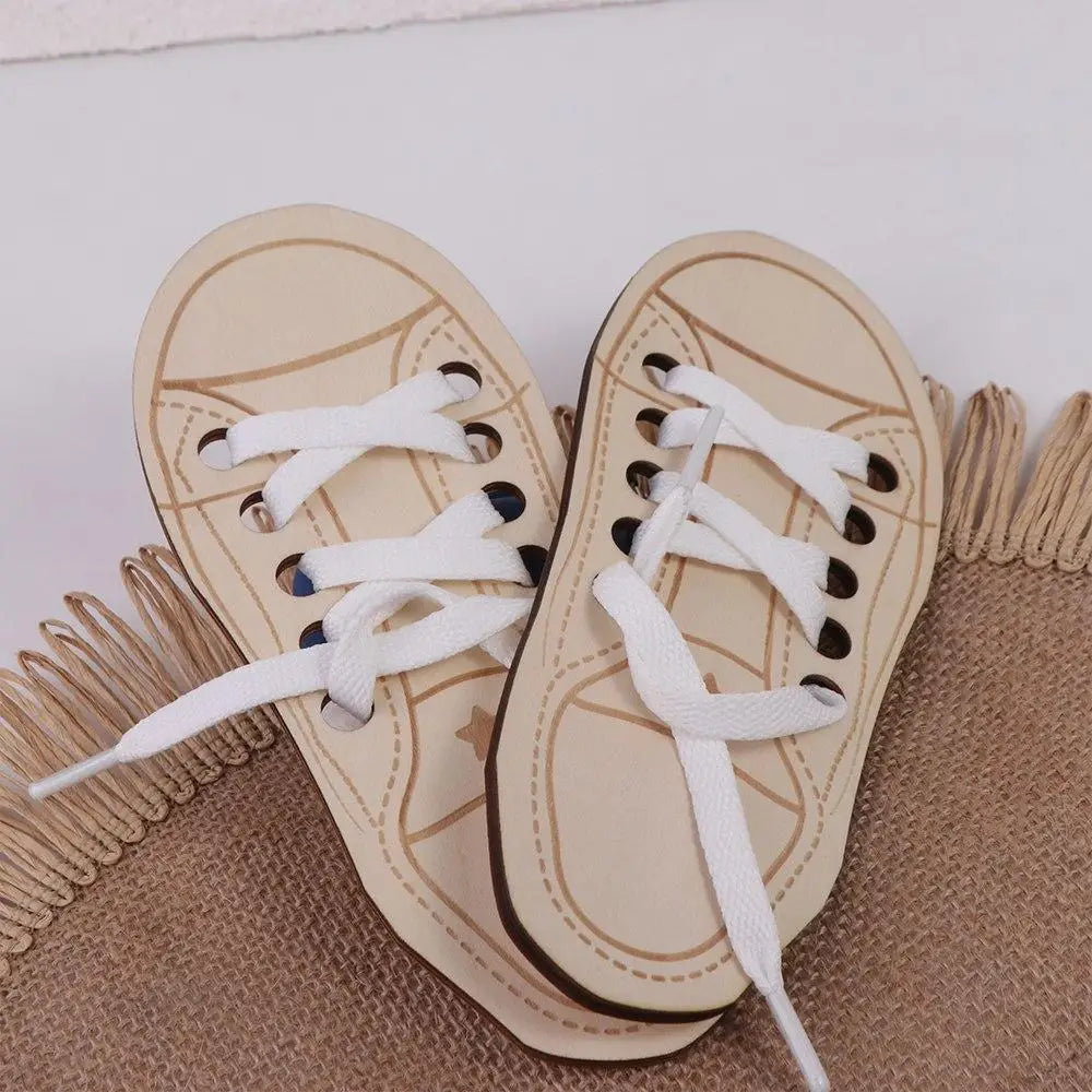 A pair of light beige wooden lacing shoes for fine motor skill development resting on a textured brown fabric.