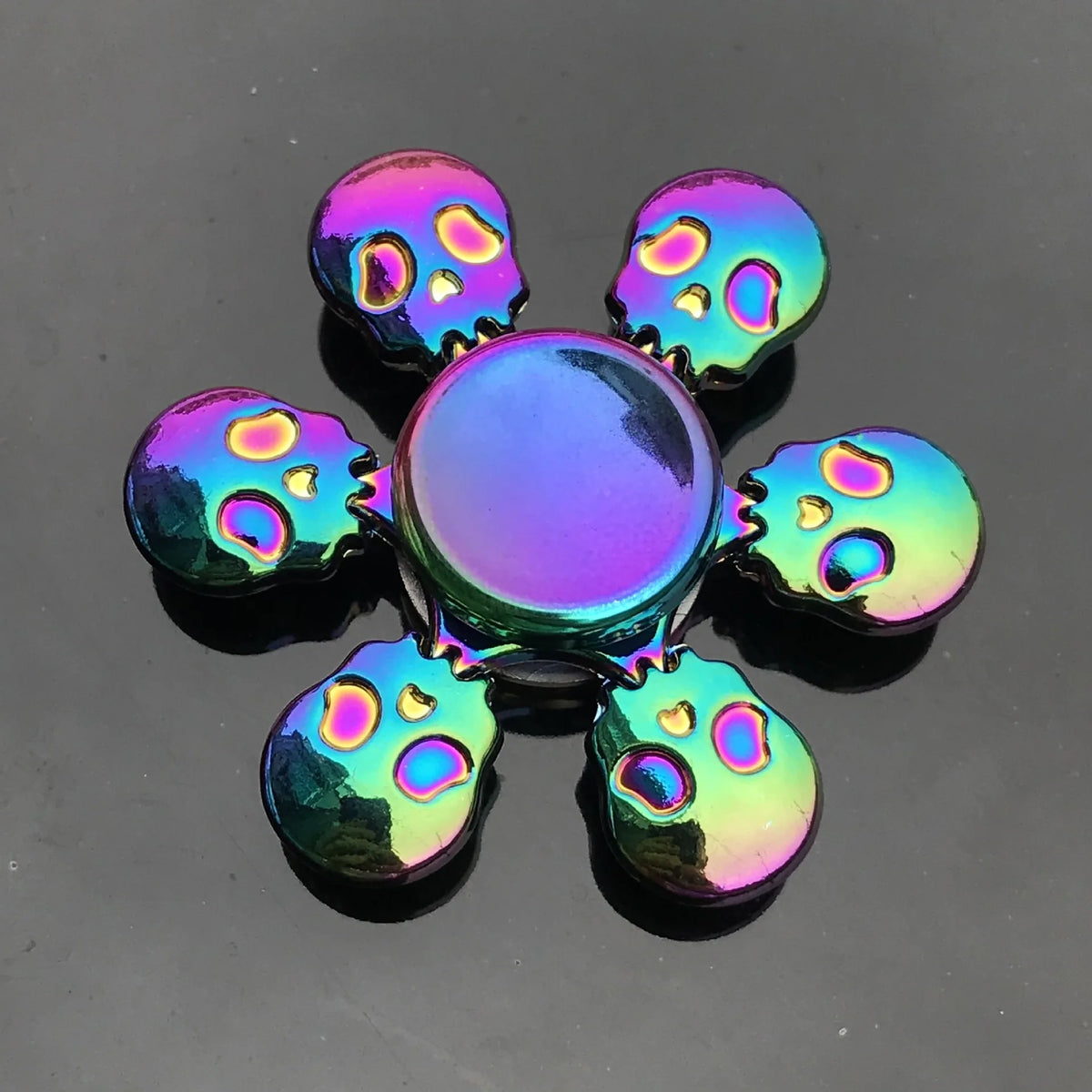 A colorful metal fidget spinner featuring a central disc and eight surrounding skull-shaped pieces.