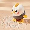A cute, yellow and gray wind-up chick toy with a pull chain resting on scattered clear plastic pieces.
