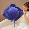 A woman holds up a purple cartoon ray devil fish plush toy against a light background.