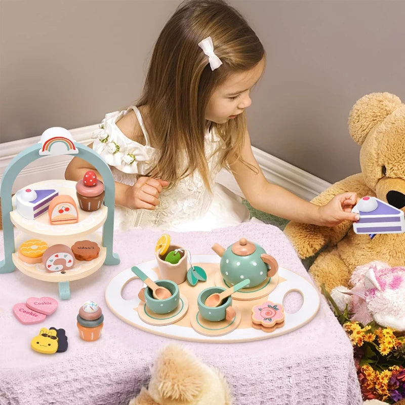 A wooden pretend play tea party set with various food items and cups is displayed on a pink tablecloth.