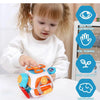 A toddler is interacting with an orange and white sensory busy board cube toy while learning hand-eye coordination and intell
